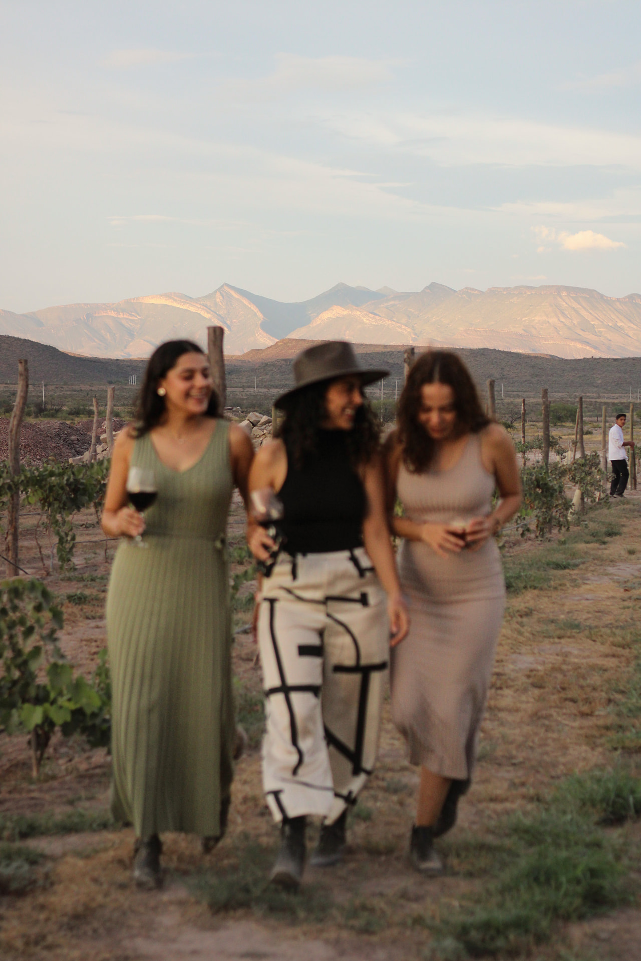 Amigas caminando entre los viñedos con copas de vino al atardecer