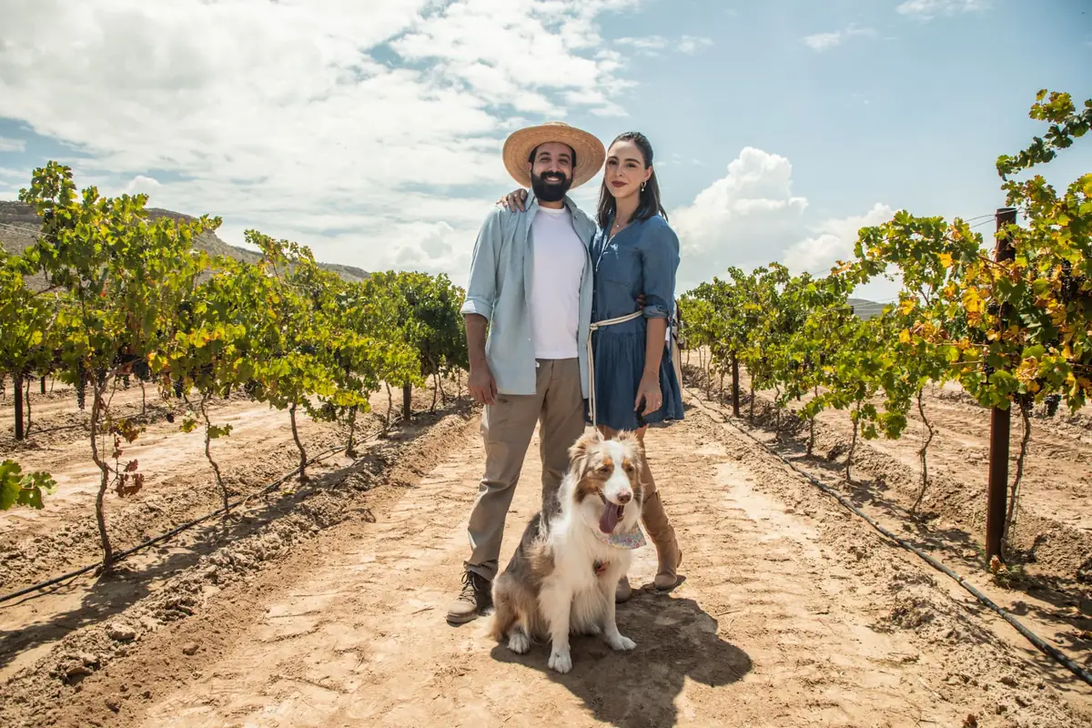 Pareja recorriendo las hileras del viñedo con su perro